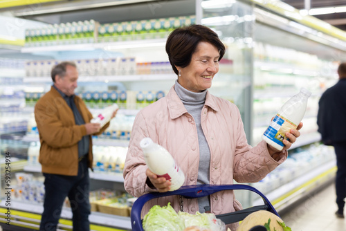 Elderly woman chooses milk in supermarket