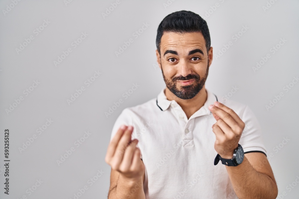 Young hispanic man with beard wearing casual clothes over white background doing money gesture with hands, asking for salary payment, millionaire business Young hispanic man with beard wearing casual clothes over white background doing money gesture with hands, asking for salary payment, millionaire business