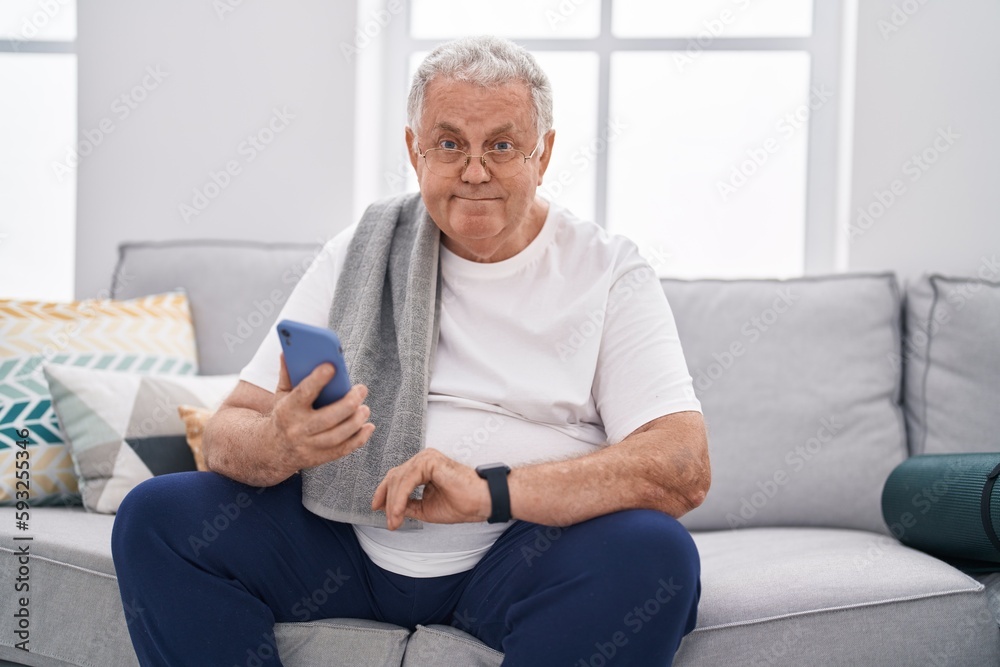 Middle age grey-haired man using smartphone looking watch at home Middle age grey-haired man using smartphone looking watch at home