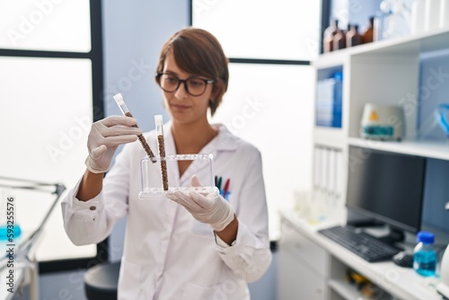 Young beautiful hispanic woman scientist holding test tubes at laboratory