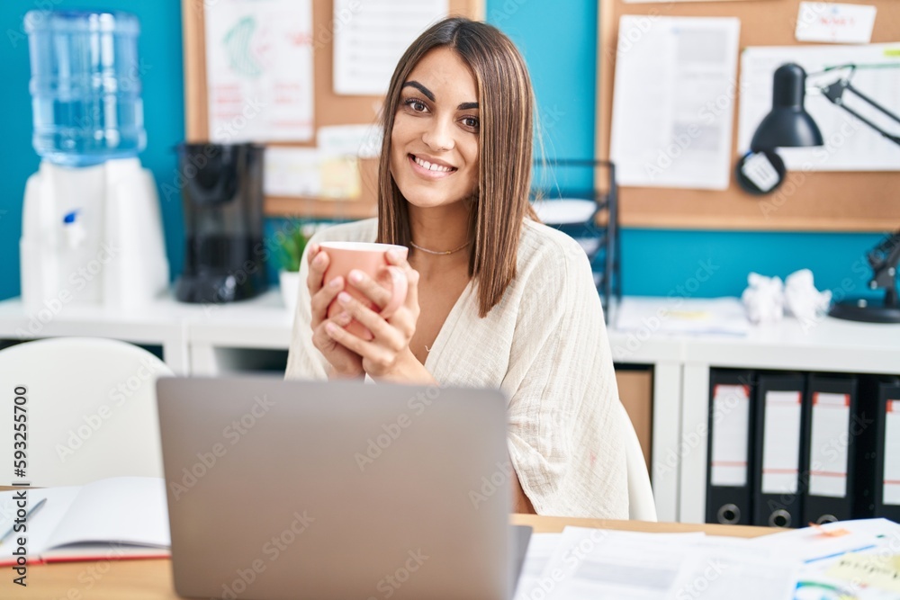 Young beautiful hispanic woman business worker using laptop drinking coffee at office