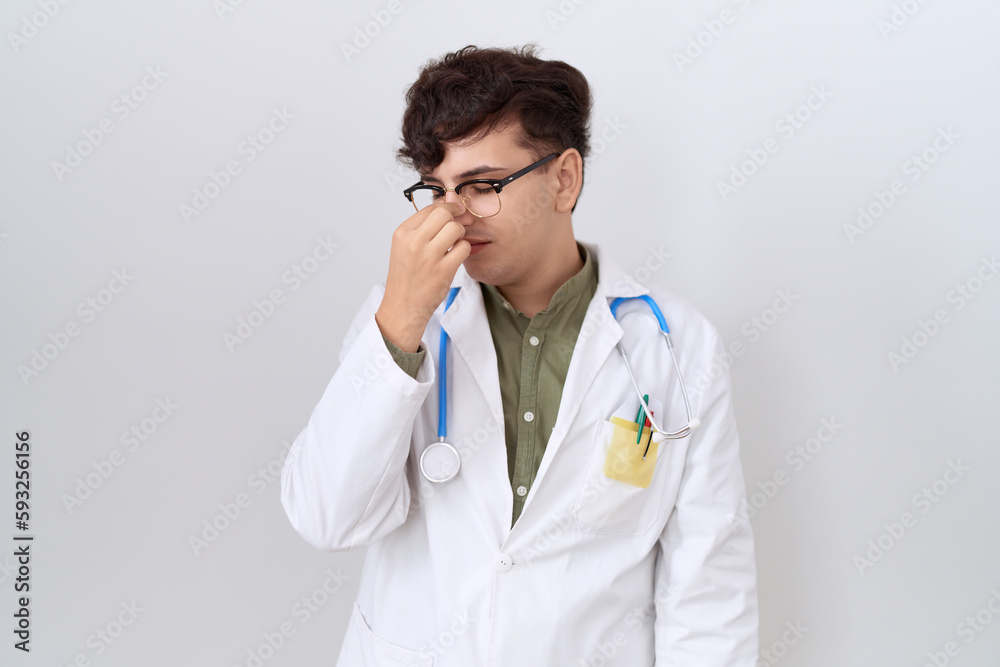 Young non binary man wearing doctor uniform and stethoscope tired rubbing nose and eyes feeling fatigue and headache. stress and frustration concept. Young non binary man wearing doctor uniform and stethoscope tired rubbing nose and eyes feeling fatigue and headache. stress and frustration concept.