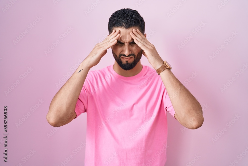 Hispanic young man standing over pink background with hand on head, headache because stress. suffering migraine. Hispanic young man standing over pink background with hand on head, headache because stress. suffering migraine.