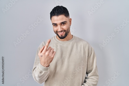 Young handsome man standing over isolated background beckoning come here gesture with hand inviting welcoming happy and smiling