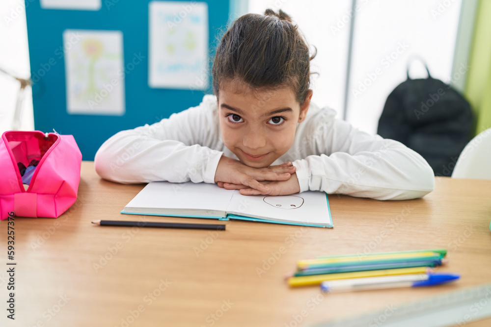 Adorable hispanic girl student sitting on table with head on book at classroom Adorable hispanic girl student sitting on table with head on book at classroom