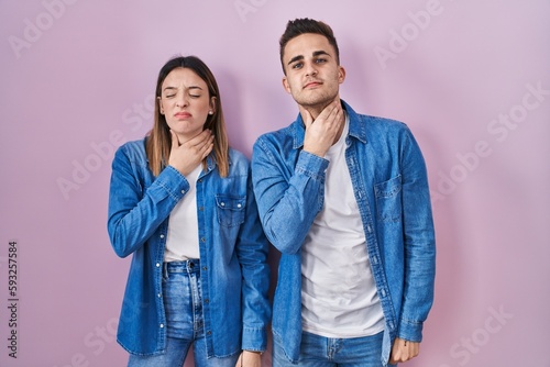 Young hispanic couple standing over pink background touching painful neck  sore throat for flu  clod and infection