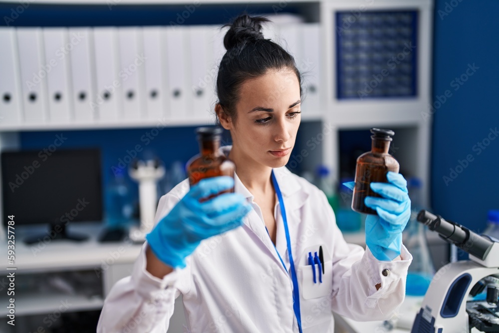 Young caucasian woman scientist holding bottles at laboratory