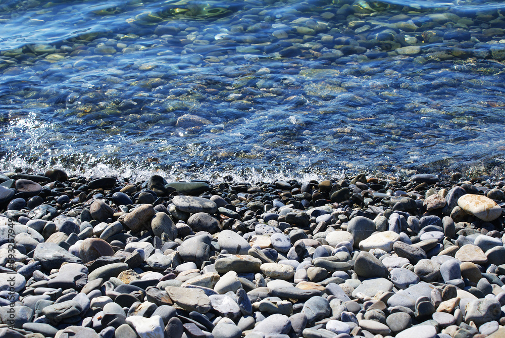 Seashore, sun glare on the water, pebbles on the seabed, nature. Background. Seashore, sun glare on the water, pebbles on the seabed, nature. Background.