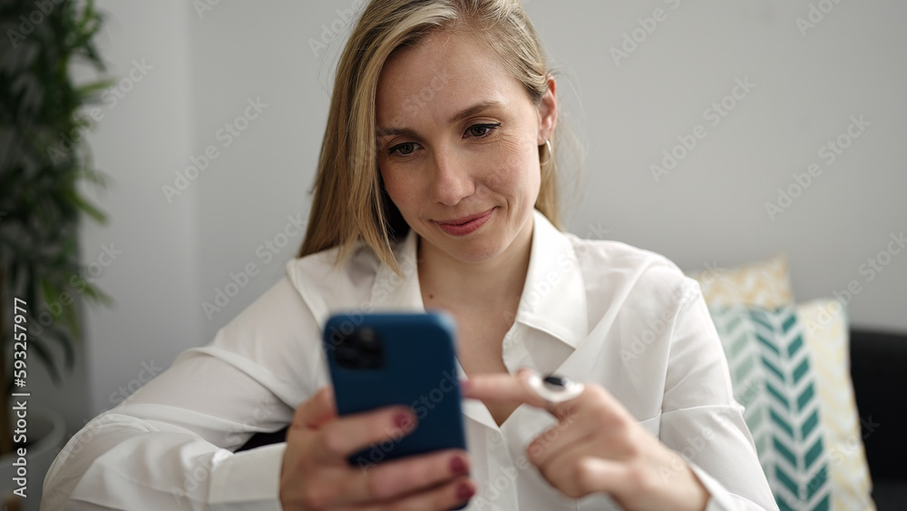 Young blonde woman using smartphone sitting on sofa at home Young blonde woman using smartphone sitting on sofa at home
