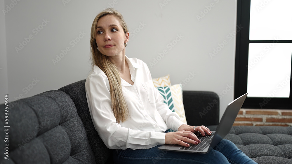 Young blonde woman using laptop sitting on sofa at home Young blonde woman using laptop sitting on sofa at home