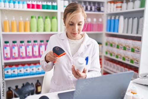 Young blonde woman pharmacist scanning pills using laptop at pharmacy