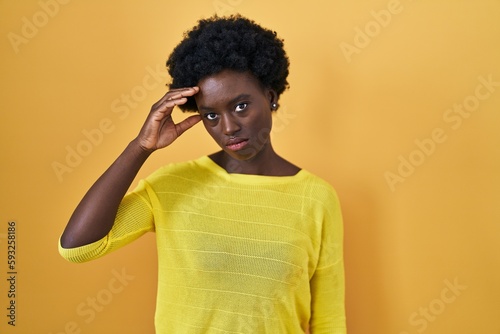 African young woman standing over yellow studio worried and stressed about a problem with hand on forehead, nervous and anxious for crisis © Krakenimages.com