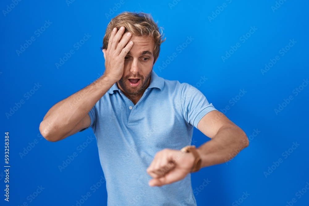 Caucasian man standing over blue background looking at the watch time worried, afraid of getting late Caucasian man standing over blue background looking at the watch time worried, afraid of getting late