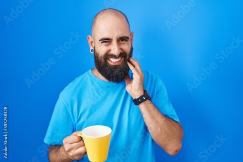 Young hispanic man with beard and tattoos drinking a cup of coffee touching mouth with hand with painful expression because of toothache or dental illness on teeth. dentist concept.