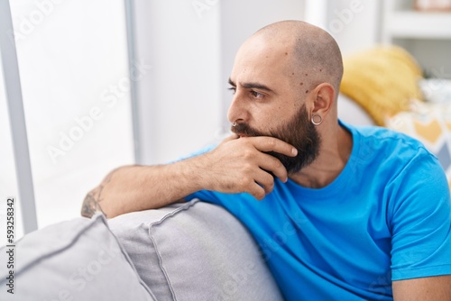 Young bald man sitting on sofa with serious expression at home