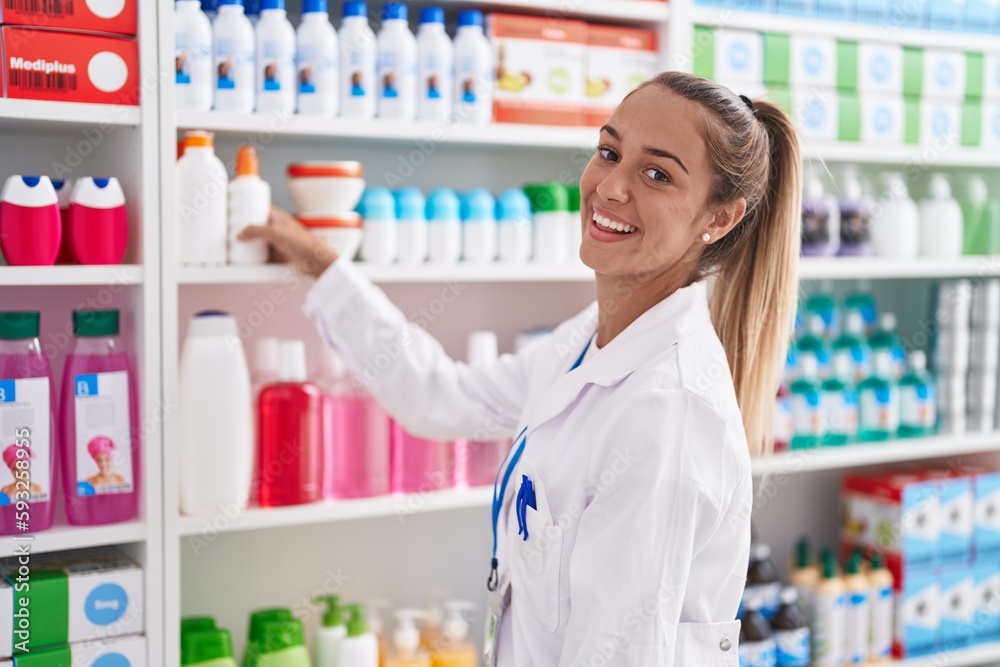 Young beautiful hispanic woman pharmacist smiling confident holding bottle at pharmacy