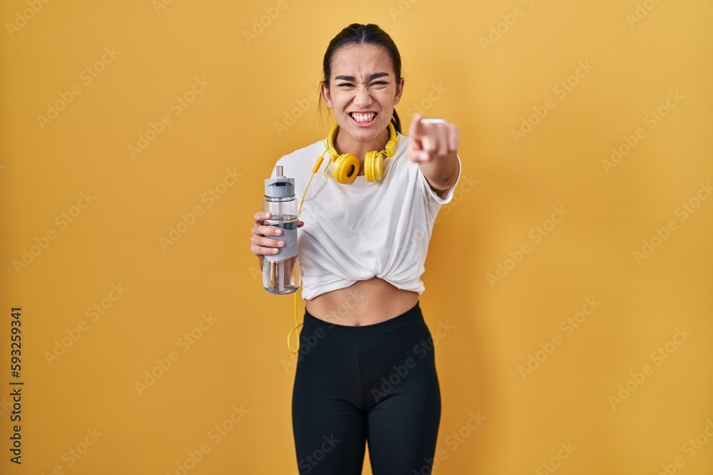 Young south asian woman wearing sportswear drinking water pointing displeased and frustrated to the camera, angry and furious with you