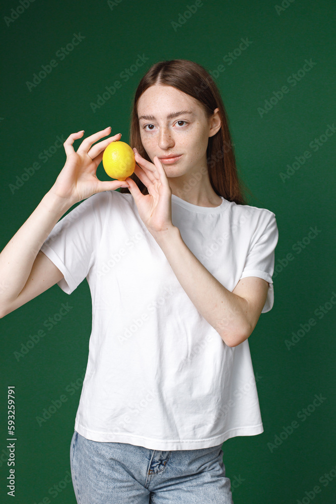 Studio portrait of a girl model holding a lemon isolated on green background