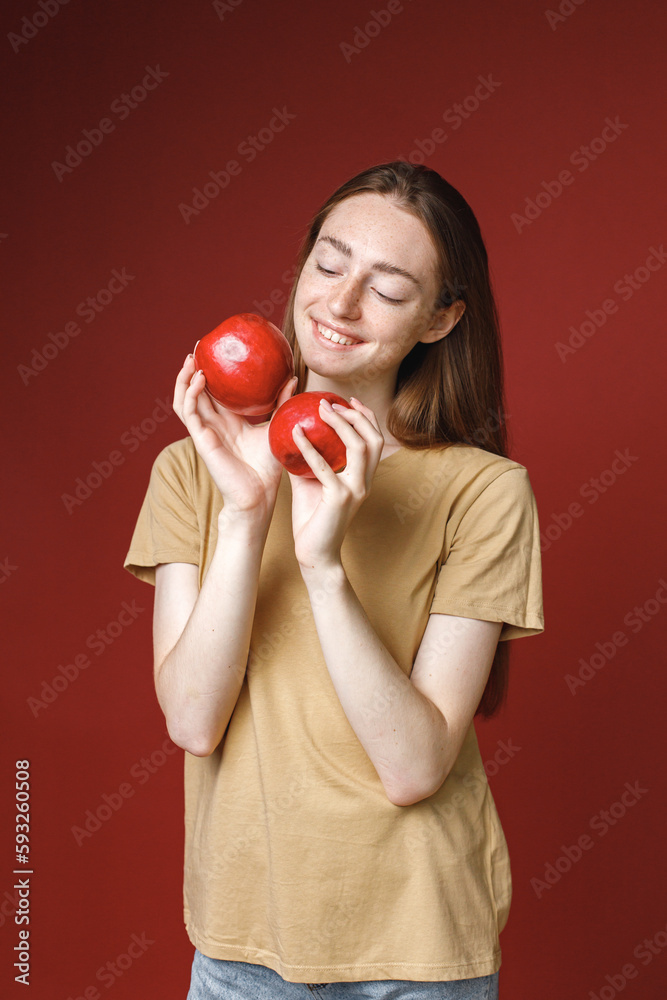 Studio portrait of a girl holding two red apples isolated on red background Studio portrait of a girl holding two red apples isolated on red background