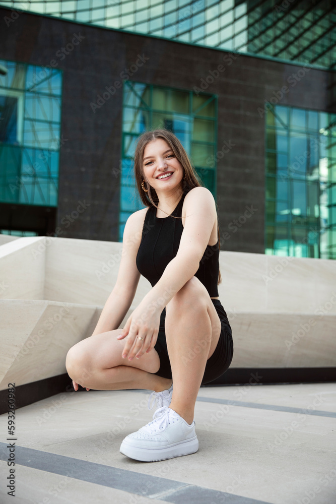 Fototapeta premium Front image of a gorgeous young woman in black top and shorts, posing with attitude outside.