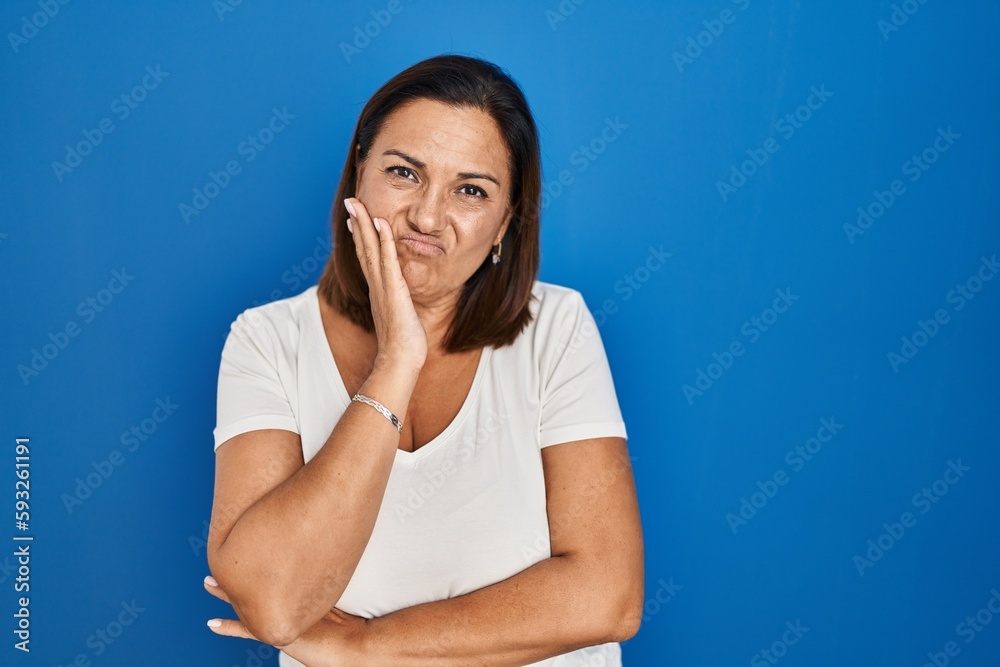 Hispanic mature woman standing over blue background thinking looking tired and bored with depression problems with crossed arms. Hispanic mature woman standing over blue background thinking looking tired and bored with depression problems with crossed arms.