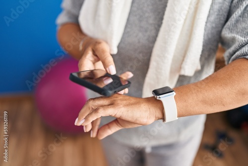 Middle age hispanic woman wearing sportswear using smartwatch and smartphone at laundry room © Krakenimages.com