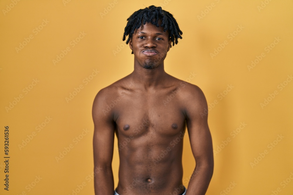 Young african man with dreadlocks standing shirtless puffing cheeks with funny face. mouth inflated with air, crazy expression.