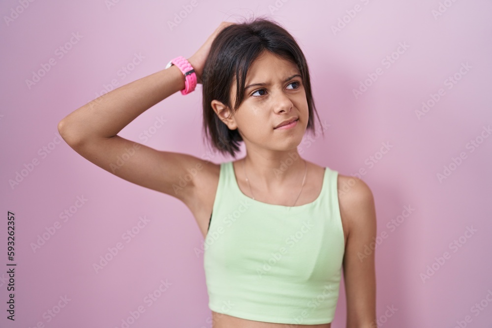 Young girl standing over pink background confuse and wondering about question. uncertain with doubt, thinking with hand on head. pensive concept. Young girl standing over pink background confuse and wondering about question. uncertain with doubt, thinking with hand on head. pensive concept.