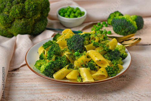 Plate with tasty penne pasta and broccoli on light wooden background