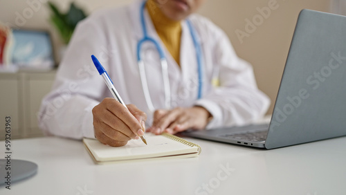 Young african american woman doctor using laptop taking notes at clinic