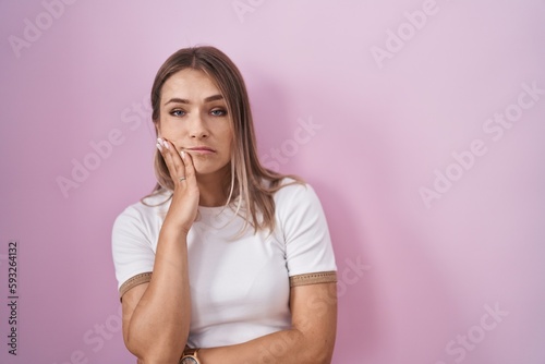Blonde caucasian woman standing over pink background thinking looking tired and bored with depression problems with crossed arms.