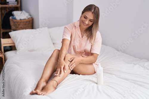 Young caucasian woman applying skin lotion treatment sitting on bed at bedroom