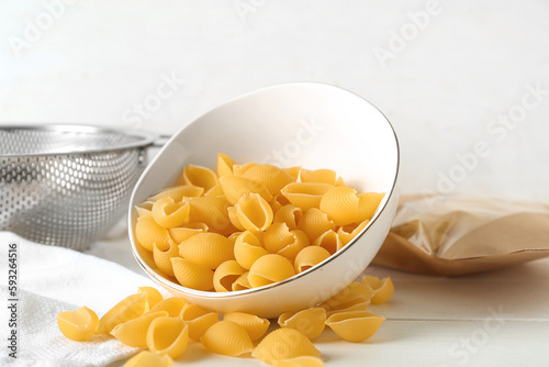 Bowl with raw conchiglie pasta on light wooden background photo