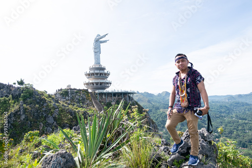 Photo of a young man standing on a hill with a statue of the Lord Jesus in Buntu Burake Toraja in the background photo
