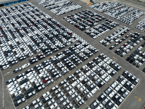 Aerial view of new cars stock at factory parking lot. Above view cars parked in a row. Automotive industry. Logistics business. Import or export new cars at warehouse. Big parking lot at port terminal