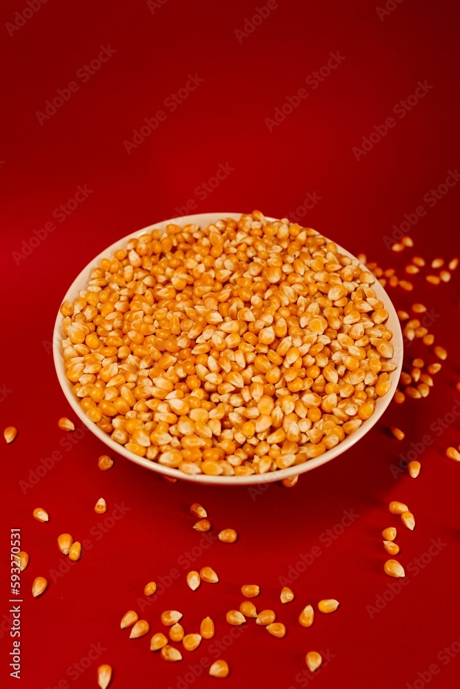 Vertical closeup of a popcorn bowl with some corns spilled around it isolated on a red background Vertical closeup of a popcorn bowl with some corns spilled around it isolated on a red background