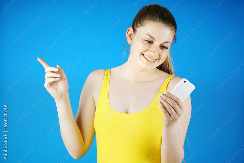 Cheerful young woman wears a yellow swimsuit and holds a smartphone mobile for chatting, texting and dating Cheerful young woman wears a yellow swimsuit and holds a smartphone mobile for chatting, texting and dating