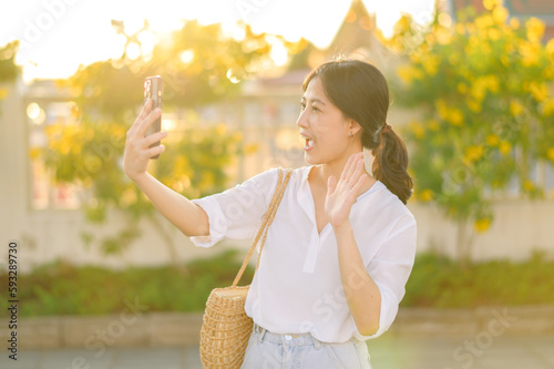 Portrait young beautiful asian woman using smartphone to video call with friend and explore street on summer vacation in Bangkok, Thailand © Jirawatfoto