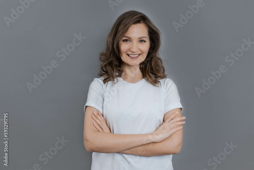 Beautiful young woman smiles and crosses her arms over her chest, looking at the camera, copy space