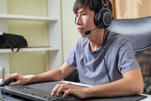 Fotografie Concentrated young Asian esport gamer man looking monitor playing computer online skills game, pay attention in competition at home