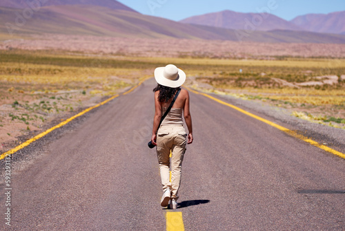rear view latina woman tourist photographer adventurer walking on the road of the altiplano in Los Flamencos National Reserve Antofagasta Region San Pedro de Atacama.