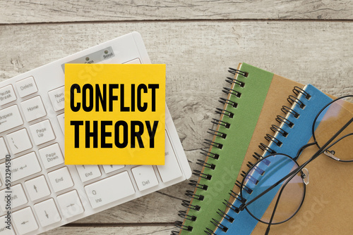 CONFLICT THEORY text on yellow sticky note attached to white keyboard