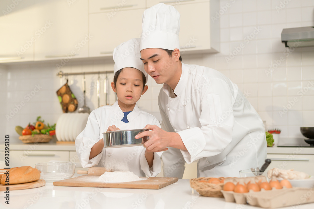 Young Asian father and his son wearing chef uniform baking together in kitchen at home Young Asian father and his son wearing chef uniform baking together in kitchen at home