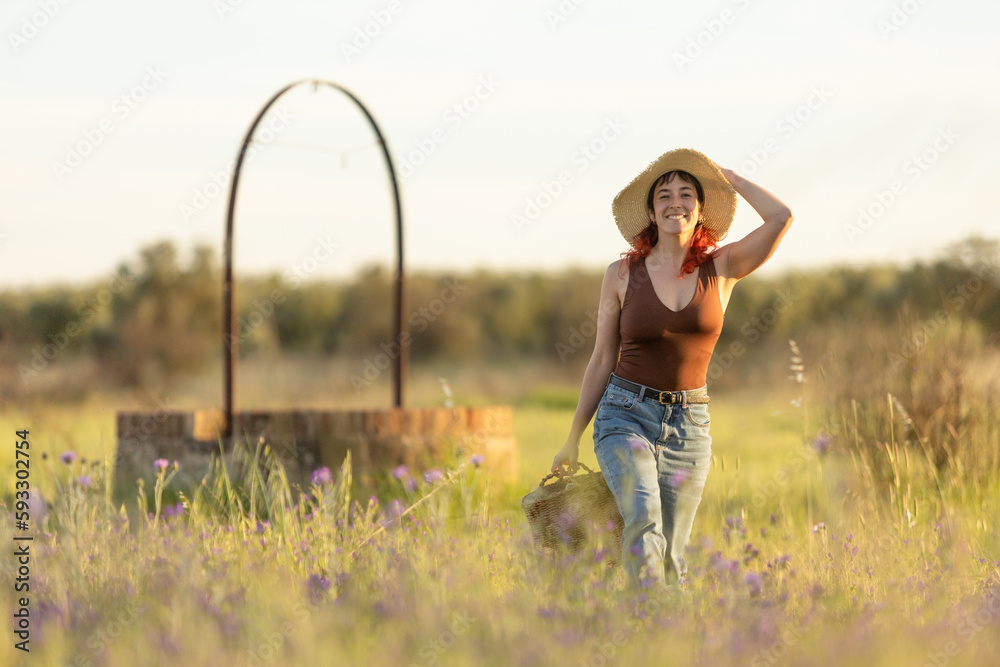 red haired woman in the meadow enjoying the sunset by a well with a wicker basket, walking on the grass red haired woman in the meadow enjoying the sunset by a well with a wicker basket, walking on the grass