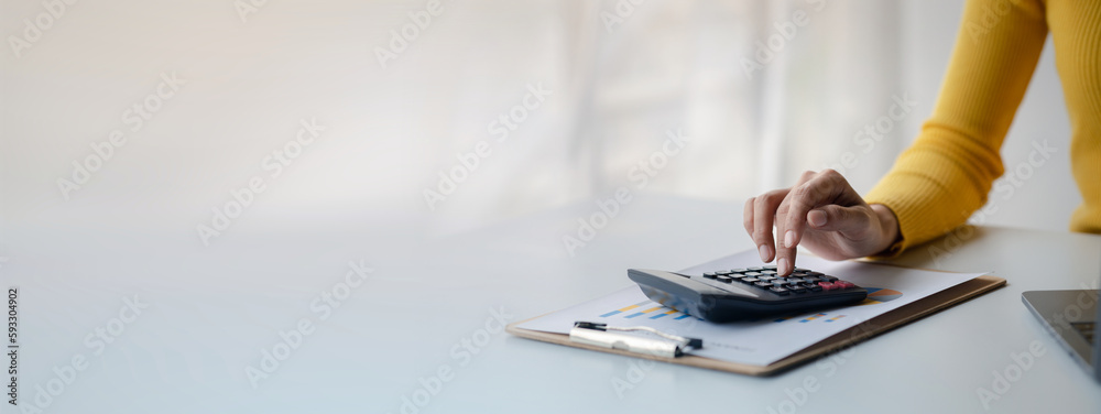 Businessman using a calculator to calculate numbers on a company's financial documents, she is analyzing historical financial data to plan how to grow the company. Financial concept. - obrazy, fototapety, plakaty 