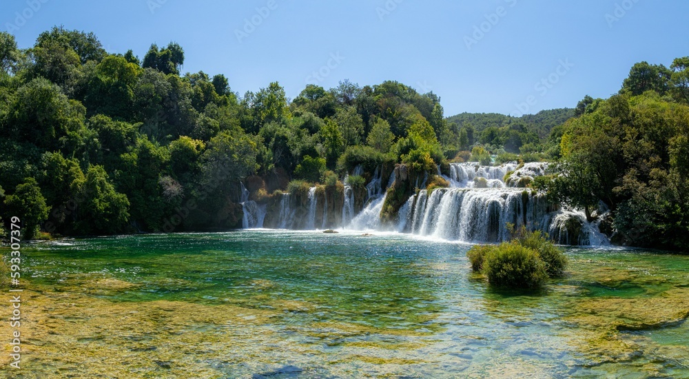 Scenic view of a waterfall flowing through green trees in Krka national park, Croatia on a sunny day Scenic view of a waterfall flowing through green trees in Krka national park, Croatia on a sunny day