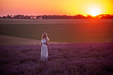 Young blonde woman stands in purple field at sunset in the bright rays of sun. Travel in countryside. Allergy concept. Sunset sky. Carefree girl with long healthy hair. human countryside lifestyle