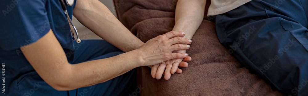 Doctor holding a sick senior patient by hand supporting her sitting in a hospital room Doctor holding a sick senior patient by hand supporting her sitting in a hospital room