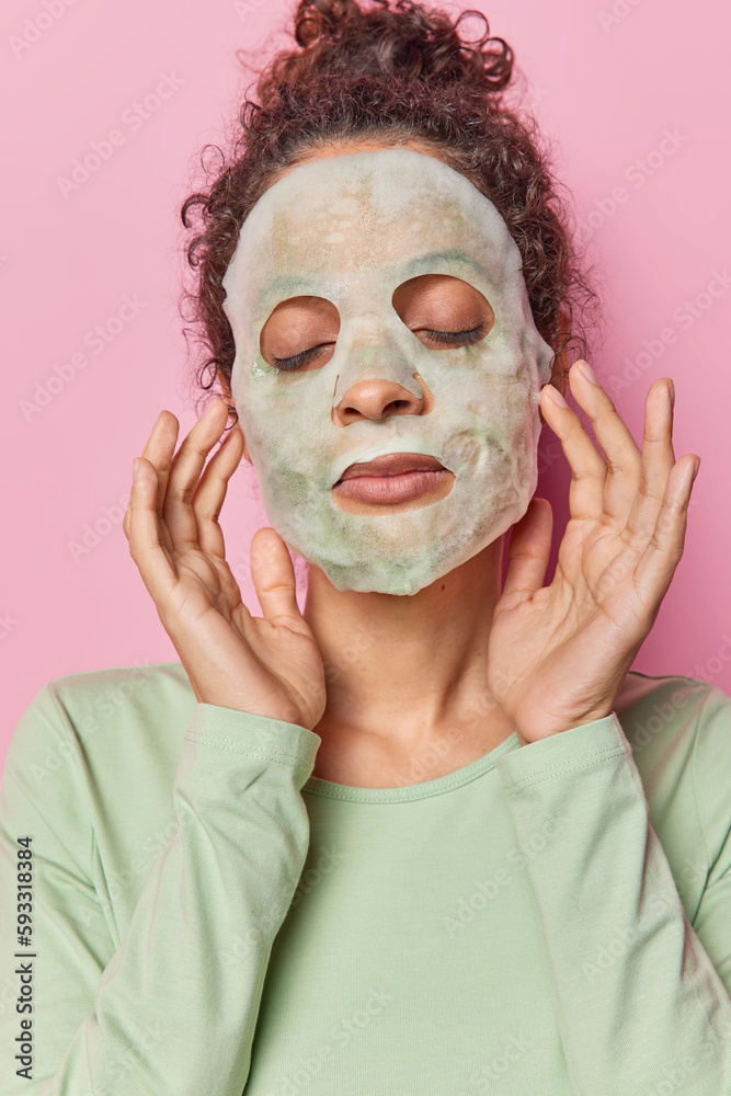 Vertical image of brunette woman applies purifying bubble beauty mask keeps eyes closed undergoes daily skin care routines wears casual jumper poses against rosy studio wall. Wellness concept Vertical image of brunette woman applies purifying bubble beauty mask keeps eyes closed undergoes daily skin care routines wears casual jumper poses against rosy studio wall. Wellness concept