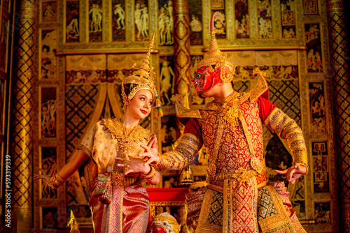 Beautiful Asian woman wear Thai traditional dress action of dancing together with Thai classic masked from the Ramakien character with Thai painting on public place wall.